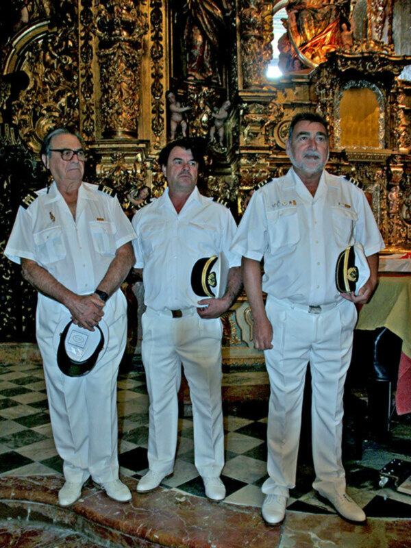 Tres hombres en uniforme blanco posan frente a un altar ornamental en una iglesia.