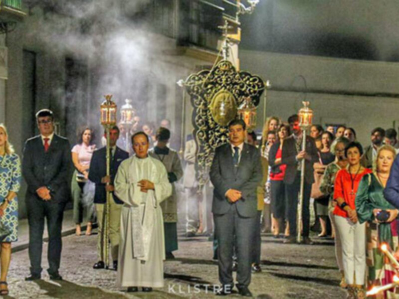 Procesión nocturna con procesionarios y velas, iluminada por la luna y el humo.