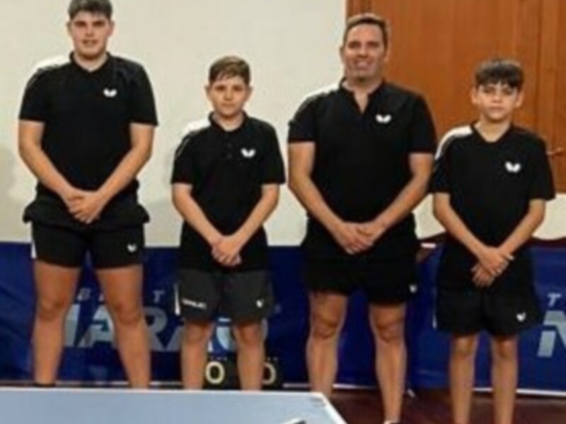 Equipo de tenis de mesa con entrenador y jugadores en una sesión de entrenamiento.