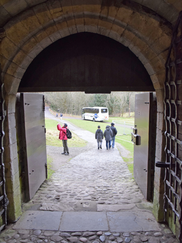 Turistas explorando un camino medieval a través de una puerta de arco en un castillo o fortaleza histórica.