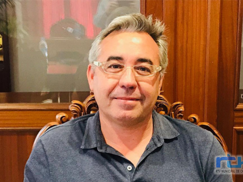 Retrato de hombre con gafas, sentado en un sillón de madera, en un entorno formal.