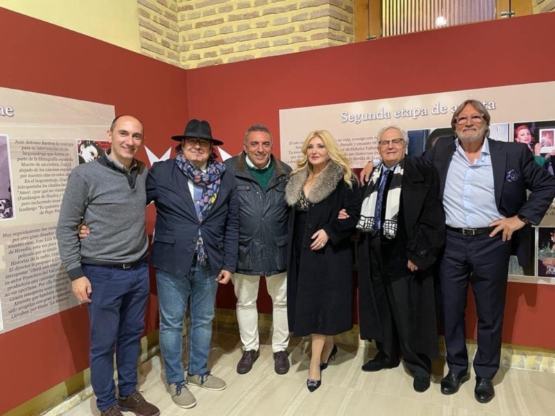 Grupo de personas posando en una exposición con un fondo rojo y blanco.