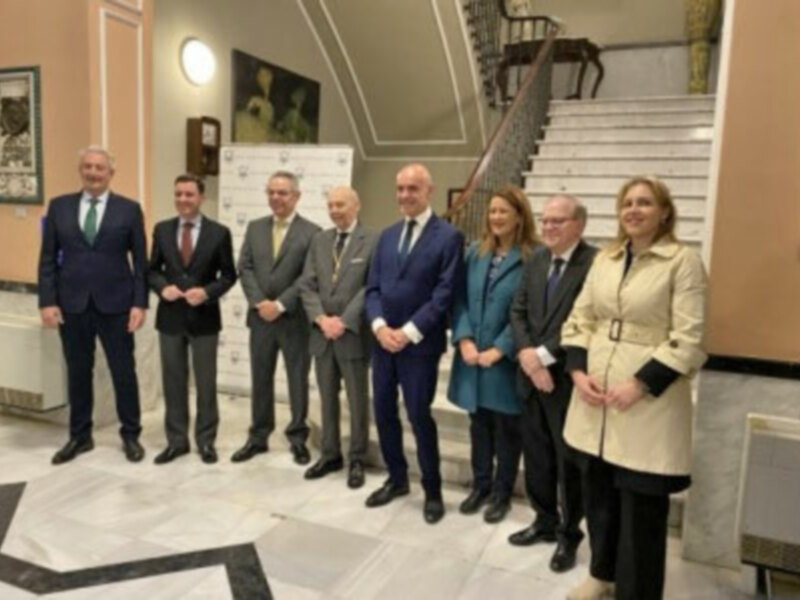 Gruppo di persone in abiti formali posano per una foto in un ambiente elegante con scale e decorazioni classiche.
