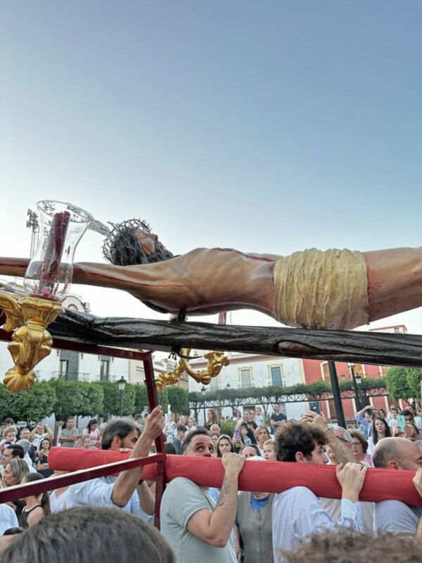 Procesión religiosa con una imagen de Jesús portada por fieles en una plaza urbana.