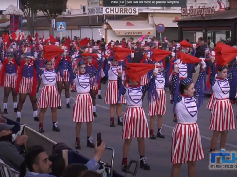 Desfile de jóvenes bailarinas en trajes patrióticos con banderas españolas, celebrando en Chipiona.
