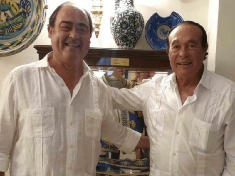 Dos hombres sonrientes en una sala decorada con cerámica tradicional.