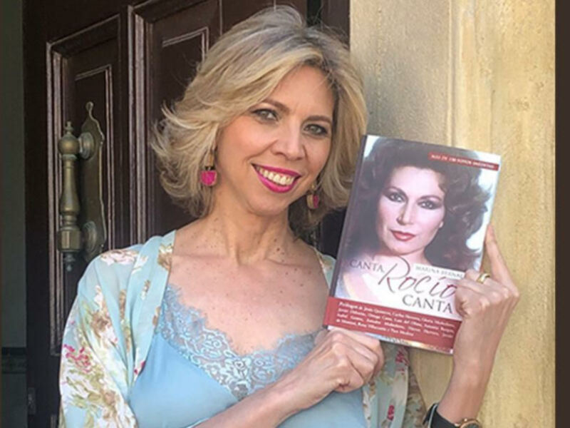 Una mujer con cabello rubio y flecos celebra sostiene un libro titulado 'Rocío Canta'.