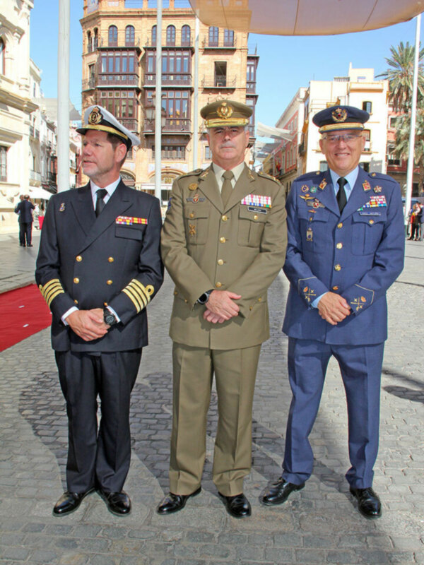 Tres oficiales militares en uniforme posan para una foto en una calle con edificios históricos y palmeras al fondo.