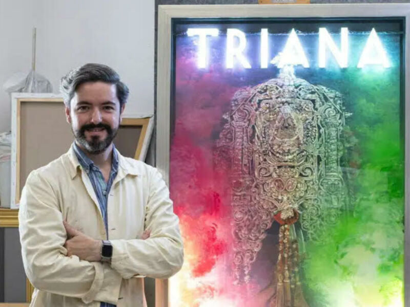 Un artista posa orgulloso junto a su obra de arte, que muestra un diseño abstracto con colores vibrantes y un texto en el centro.