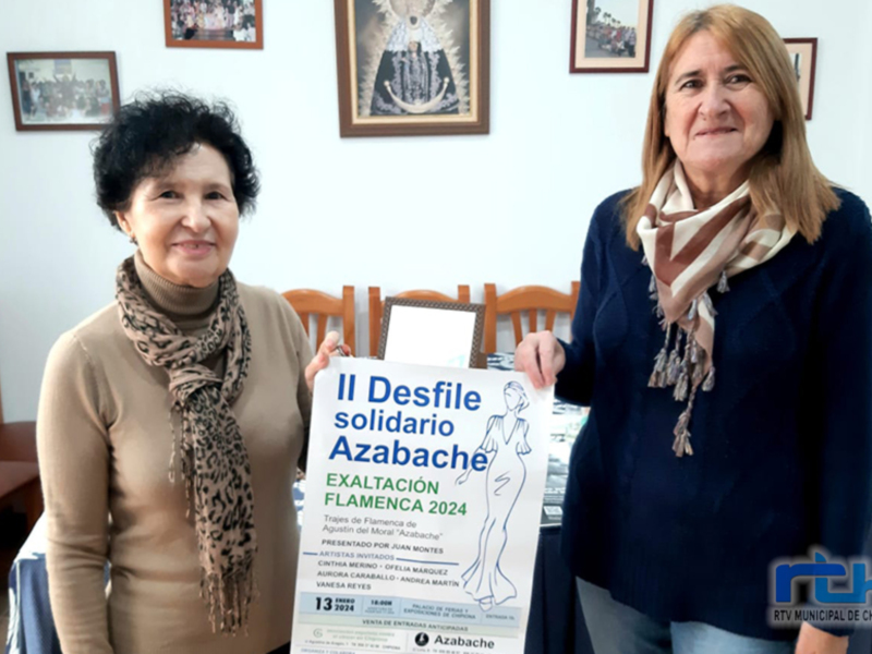 Dos mujeres posan con un cartel anunciando el II Desfile Solidario Azabache, evento cultural y solidario celebrado el 13 de febrero de 2024 en Chipiona, Cádiz.
