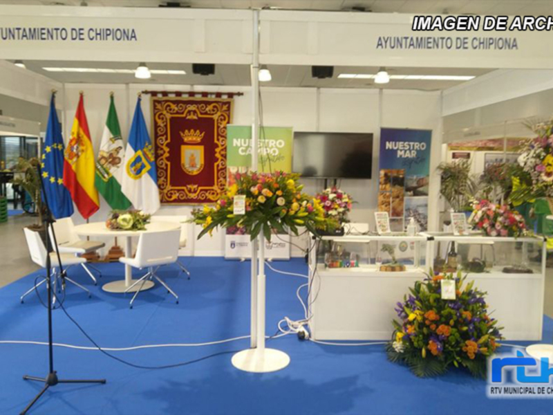 Estación de exposición del Ayuntamiento de Chipiona con banderas y flores, representando la promoción turística y cultural de la localidad.