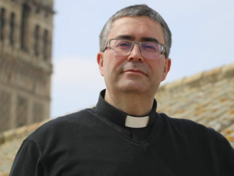 Retrato de un sacerdote frente a una catedral histórica.