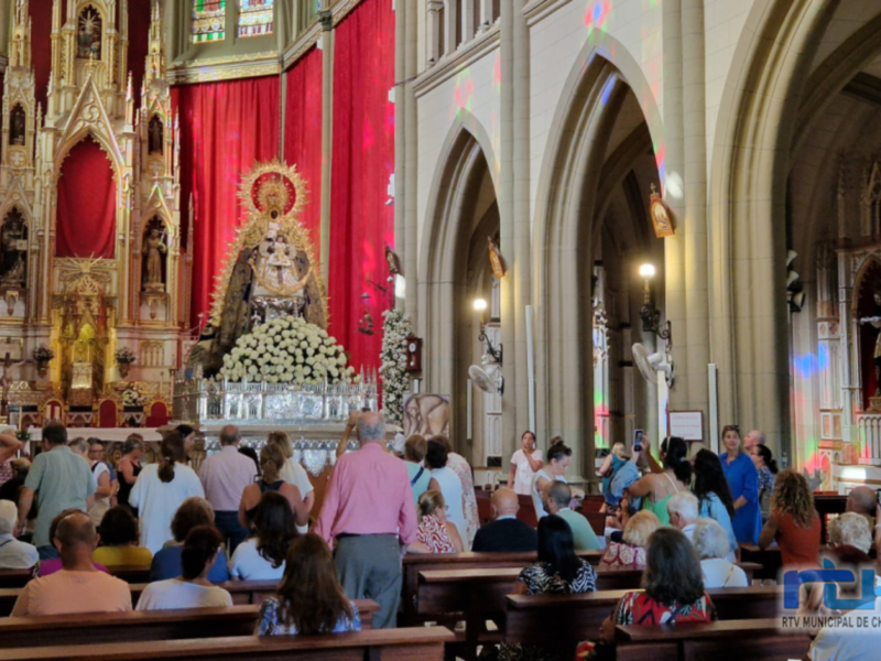 Interior de una iglesia con una imagen de la Virgen en el altar, rodeada de personas en oración y observación.