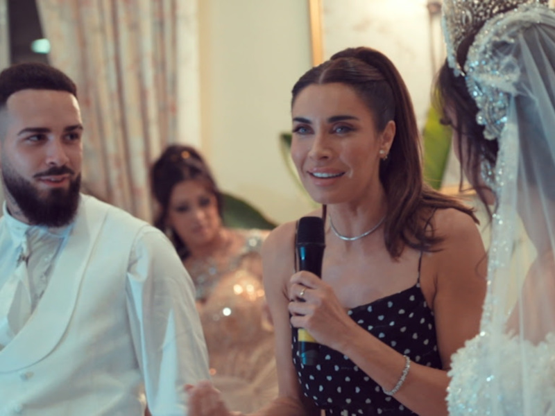 Fotografía de una boda con una pareja vestida de blanco y una mujer sosteniendo un micrófono.