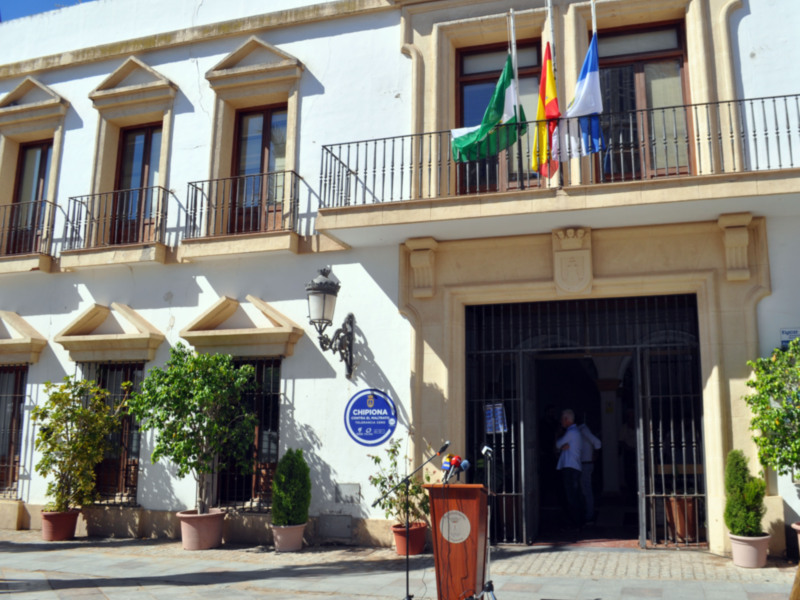 Edificio público con banderas y microfonios en la entrada.