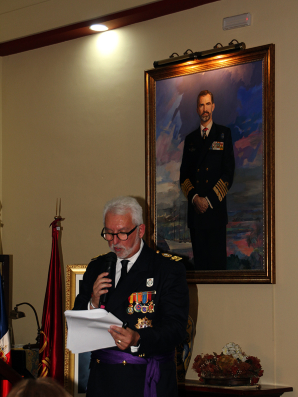 Un oficial militar en uniforme negro con insignias y medallas, luce serio mientras lee un documento en un evento formal.