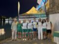 Equipo de remo celebrante en el mar nocturno, con una bandera de la Federación Andaluza de Remo en el fondo.
