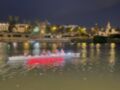 Paseo nocturno en el río Guadalquivir con barcos iluminados y palmeras en el fondo.
