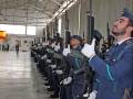 Guardias en uniforme azul con cascos, realizando una ceremonia militar dentro de un hangar industrial.